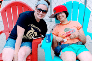 Volunteer and camper bask in the sunshine by the pool in colorful Adirondack chairs