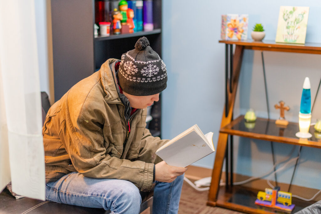 EchoingU student reads a book in a great space set up with a calming lava lamp and shelves with various items.