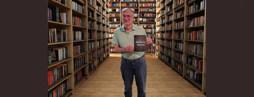 Photo of Gordon in a library holding a book of his stories. He is smiling.