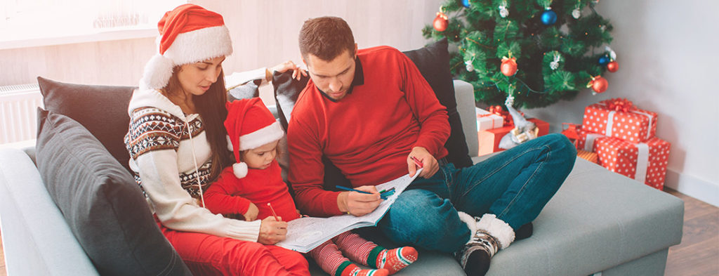 Calm Christmas with child and parents. Coloring in a book beside a Christmas Tree and gifts.