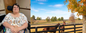 Jackie S. sitting in a flowered shirt in her wheelchair. Horses standing at a fence in the sunshine with bright blue skies and light clouds.