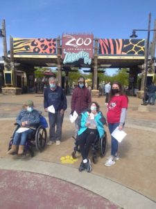 Gordon and friends at the Zoo. Standing in front of the Zoo sign smiling. Some in wheel chairs and some standing. 