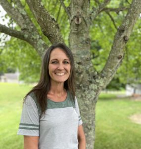 This is Dawn! She is a DSP at Echoing Hills. Wearing her company logo on a green and gray retro t-shirt shows her commitment. Dawn is smiling and has long dark hair.