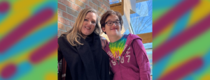 Jessie with an EchoingU student smiling in a stairwell. The student is wearing a tye dye tshirt and Jessie is in black. she has blonde hair. the student wears glasses.
