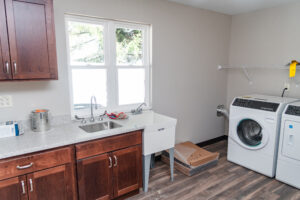 Interior shows large laundry room space with wood look floors and light colored walls.