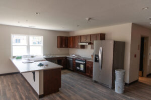 Interior shows large kitchen and gathering space with wood look floors and light colored walls.
