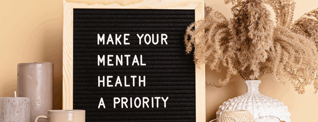 Picture in a frame that says Make Mental Health A Priority. There are calming tan colored candles and a white vase with beige colored feathers.