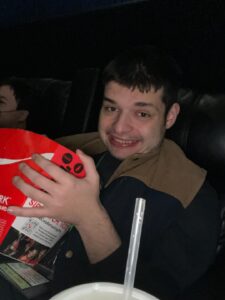 Smiling and having fun at the movies. Eating popcorn from a big red tub!